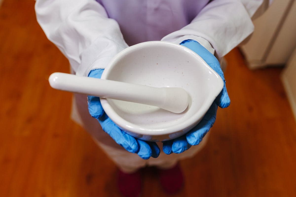 Almofariz e pistilo nas mãos de profissional com luvas — manipulação de fórmulas